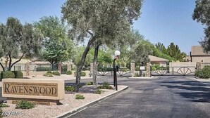 A gated entrance to Ravenswood with a sign, a lamp post, and a clear sky.