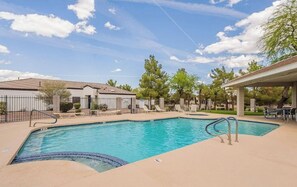 A swimming pool with lounge chairs and a covered seating area, surrounded by trees and a building with a tiled roof. - Phoenix Valley Stay (PHOENIX)