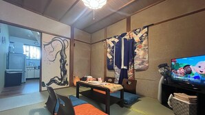 A traditional Japanese-style living room with tatami flooring, a low table, and a television displaying a cartoon. - 8 minutes walk to Sanjo station/12mins walk to GION (京都市左京区聖護院蓮華蔵町)
