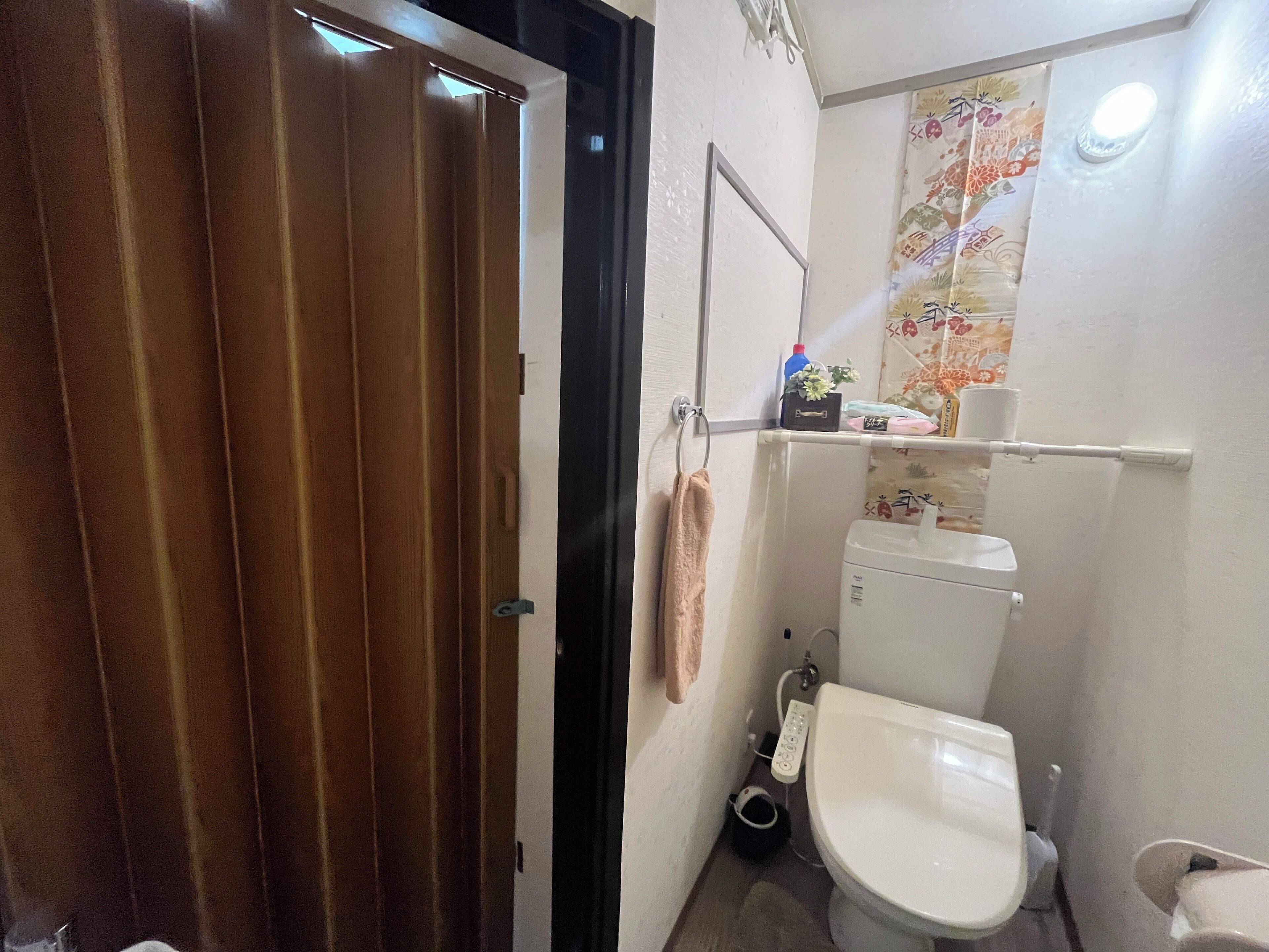 A small bathroom with a toilet, a sink, and a shower. There is a towel hanging on the wall and a small shelf with toiletries.