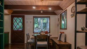 A cozy room with a wooden ceiling, a dining table with chairs, a bench, and a large window with a view of trees. - Fog & Fern Hideaway - Cozy Cabin w/ Private Hot Tub near Mt. Rainier (Ashford)