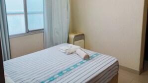 A hotel room with a bed, a window with curtains, a radiator, and a small table with a towel. - Valença Space - in the heart of the historic center (Centro Histórico Porto Alegre)