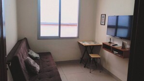 A small living room with a brown sofa, a small table, a TV on the wall, and a window. - Valença Space - in the heart of the historic center (Centro Histórico Porto Alegre)