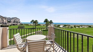 A balcony with a table and chairs, overlooking a beach and a golf course. - 211 Sailmaker ~ Ocean Sunrise (Fernandina Beach)