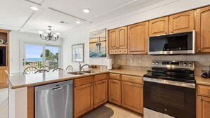 A modern kitchen with wooden cabinets, stainless steel appliances, and a view of the ocean. - 211 Sailmaker ~ Ocean Sunrise (Fernandina Beach)