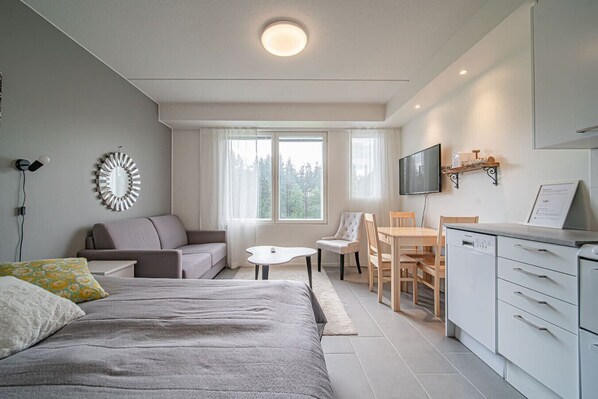 Una habitación moderna y luminosa con cama, sofá, mesa de comedor, sillas y una zona de cocina.