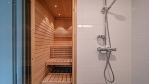 Un sauna avec des bancs en bois et un espace douche équipé d’un pommeau de douche mobile.