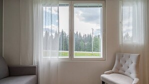 Une pièce avec une grande fenêtre, une chaise blanche et un canapé gris.