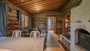 A log cabin interior with a wooden ceiling, a fireplace, a sofa, and a dining table.