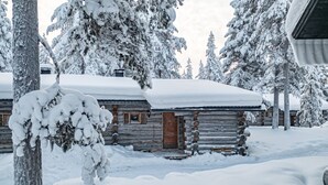 A log cabin with a snow-covered roof, surrounded by snow-laden trees.
