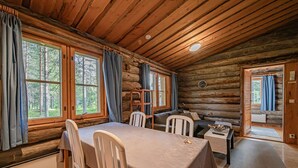 A log cabin with a dining area, a sofa, and a view of the forest.
