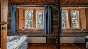 A log cabin bedroom with two beds, wooden floors, and large windows with curtains.