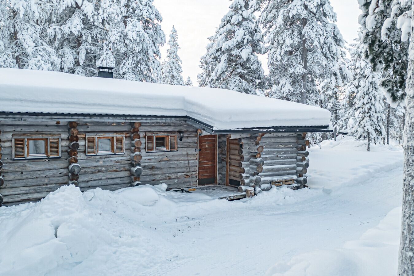 A log cabin with a snow-covered roof, wooden shutters, and a wooden door.