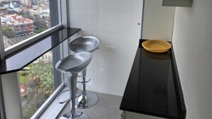 Una cocina moderna con un ventanal grande, dos taburetes de bar y una encimera negra.