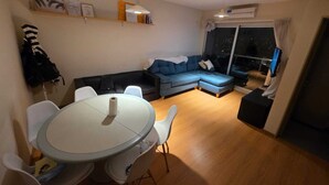 Una sala de estar moderna con una mesa de comedor redonda, sillas blancas, un sofá azul y un ventanal con vista a la ciudad de noche.