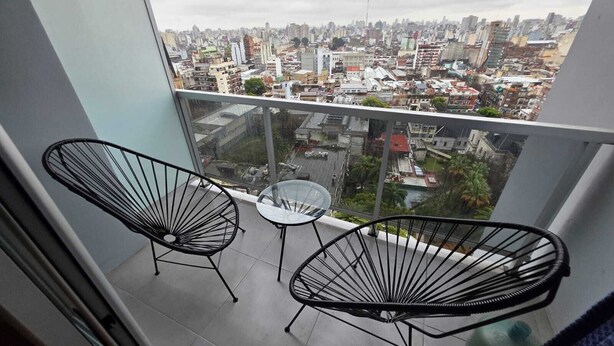 Un balcón con dos sillas negras de metal y una mesita, con vistas a un paisaje urbano.