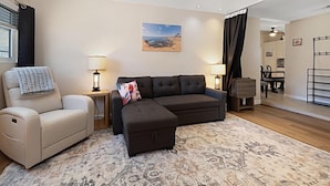 A living room with a beige sofa, a black sofa, a patterned rug, and a painting of a landscape.