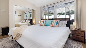 A modern bedroom with a large bed, a mirror, a nightstand, and a window with curtains.