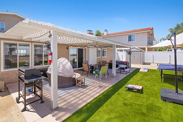 Un patio couvert avec un barbecue, des sièges d’extérieur et une table de ping-pong.