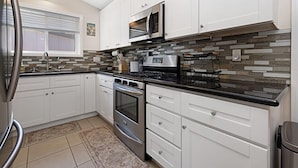 A kitchen with white cabinets, a stainless steel refrigerator, a microwave, and a stove.