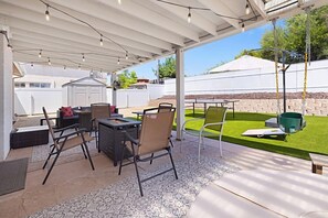 Une terrasse extérieure dotée d’un espace salon couvert, d’un barbecue et d’une chaise suspendue.