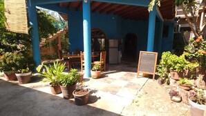 A covered patio area with potted plants, a table with chairs, and a signboard. - La Casa Del Sueño (Mazunte)