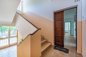 Un escalier avec une rampe en bois menant à une porte sur laquelle est posé un paillasson avec l’inscription « BIENVENUE ».