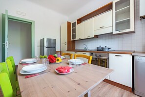 Une cuisine moderne avec des meubles blancs, un plan de travail en bois et une table à manger dressée avec des assiettes, des couverts et des fruits.
