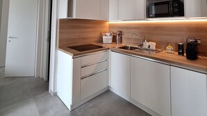 Moderni keittiö, jossa on valkoiset kaapit, puinen työtaso, mikroaaltouuni, pesuallas ja kahvinkeitin.