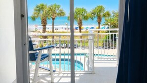 A pool area with a view of the beach, palm trees, and a clear blue sky. - Ocean blue Paradise, Perfect Location. (Myrtle Beach)