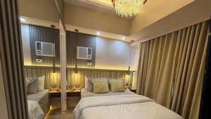 A hotel room with a large bed, a smaller bed, and a desk. There are air conditioning units on the wall and a chandelier.