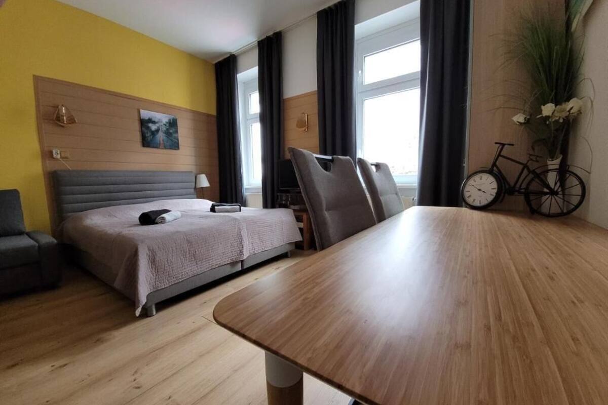A hotel room with a bed, a desk, a bicycle, and a window with curtains.