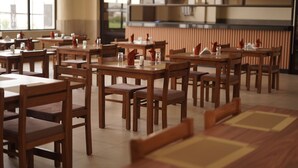 A restaurant with wooden tables and chairs, large windows, and a modern kitchen in the background.