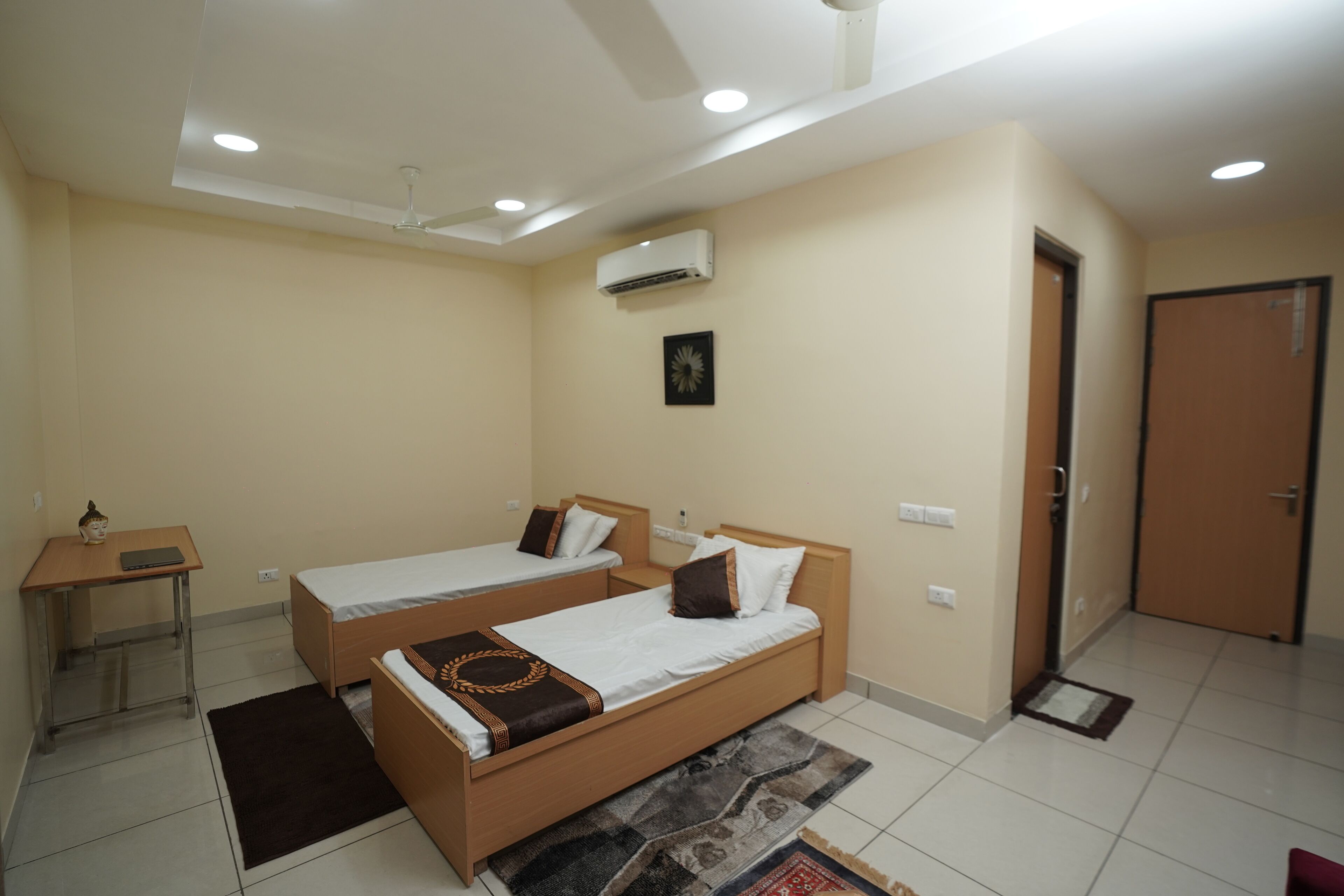 A hotel room with two single beds, a desk, an air conditioning unit, and a door.
