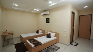 A hotel room with two single beds, a desk, an air conditioning unit, and a door.