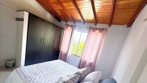 Un dormitorio con cama, armario, ventana con cortinas y techo de madera.