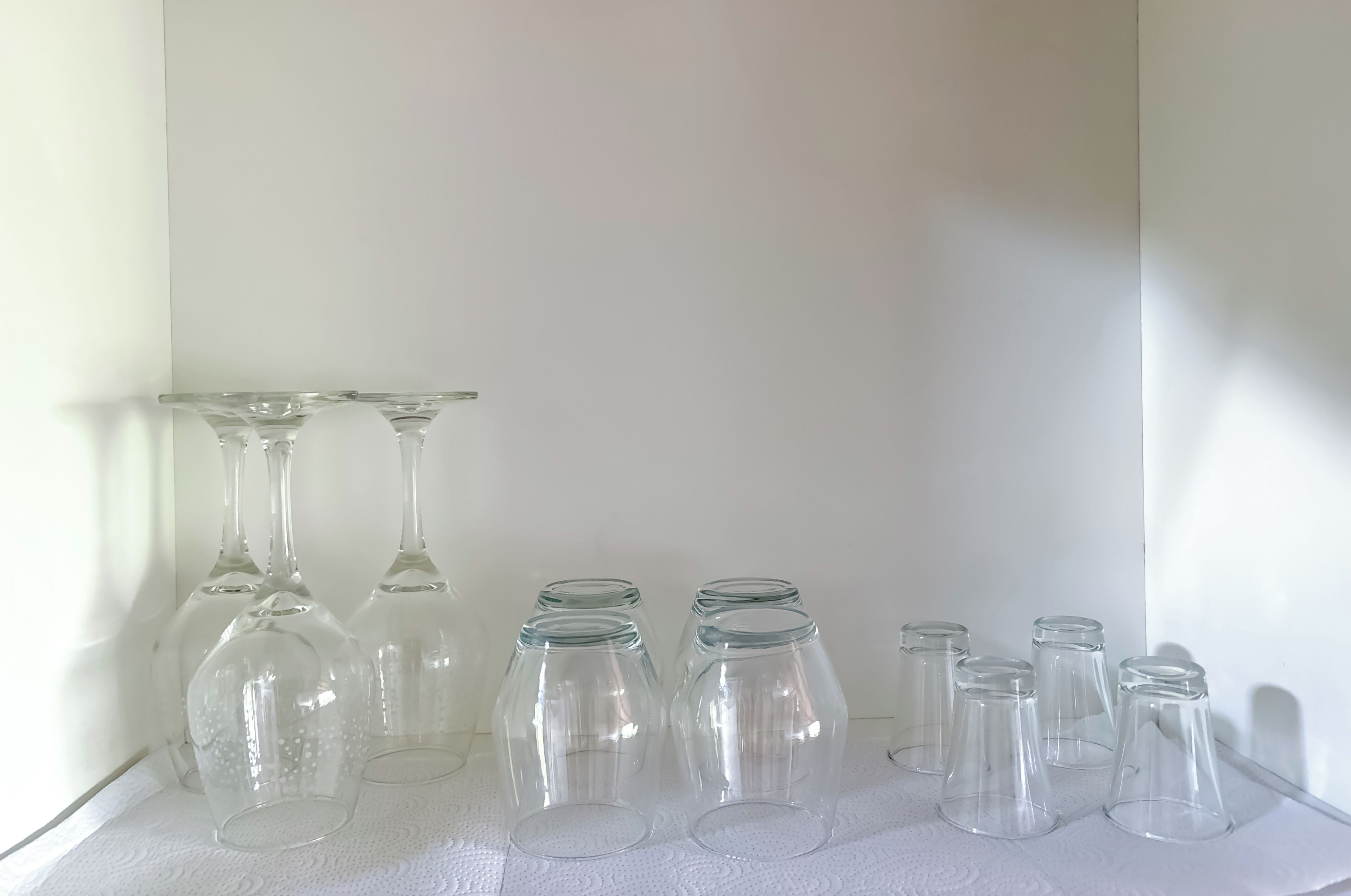 Varias copas de vino vacías dispuestas sobre una superficie blanca frente a una pared lisa.