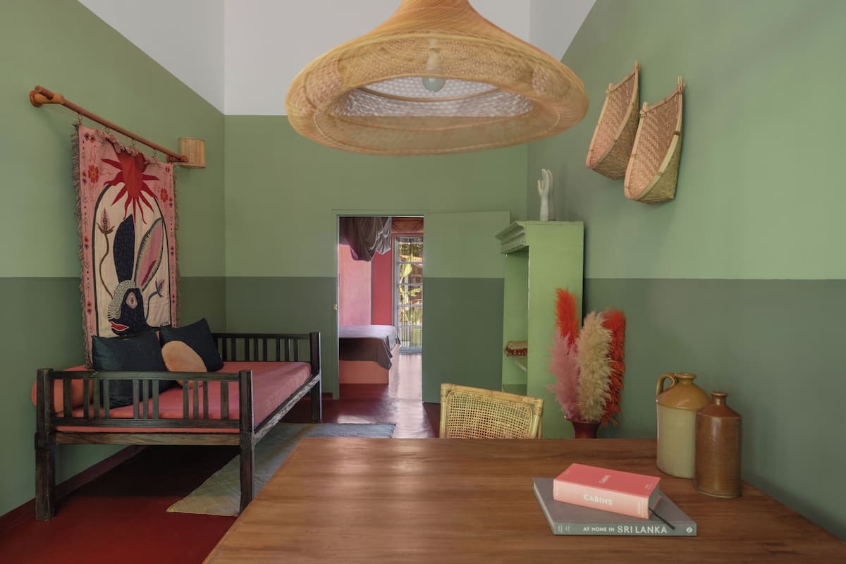 Una habitación con una cama de madera, una mesa de comedor con un libro, una lámpara colgante y vistas a otra habitación.