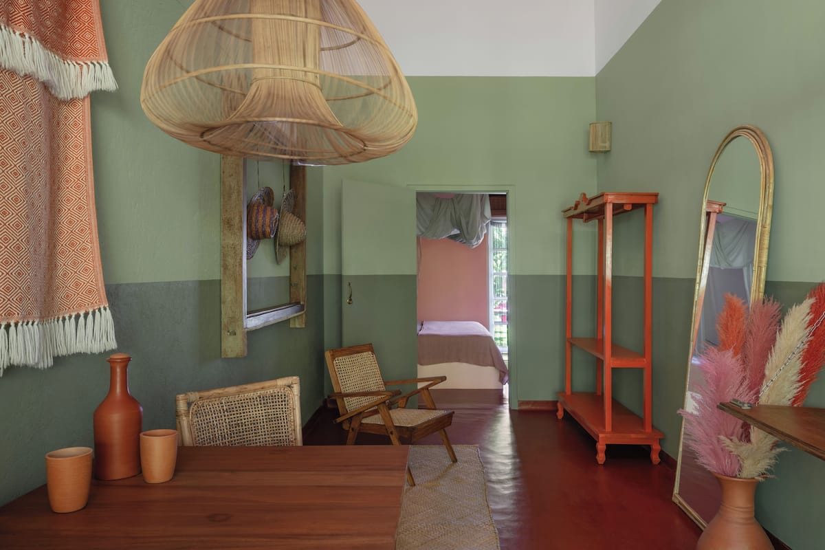 Una habitación con una mesa de madera, una silla de mimbre y un espejo grande.