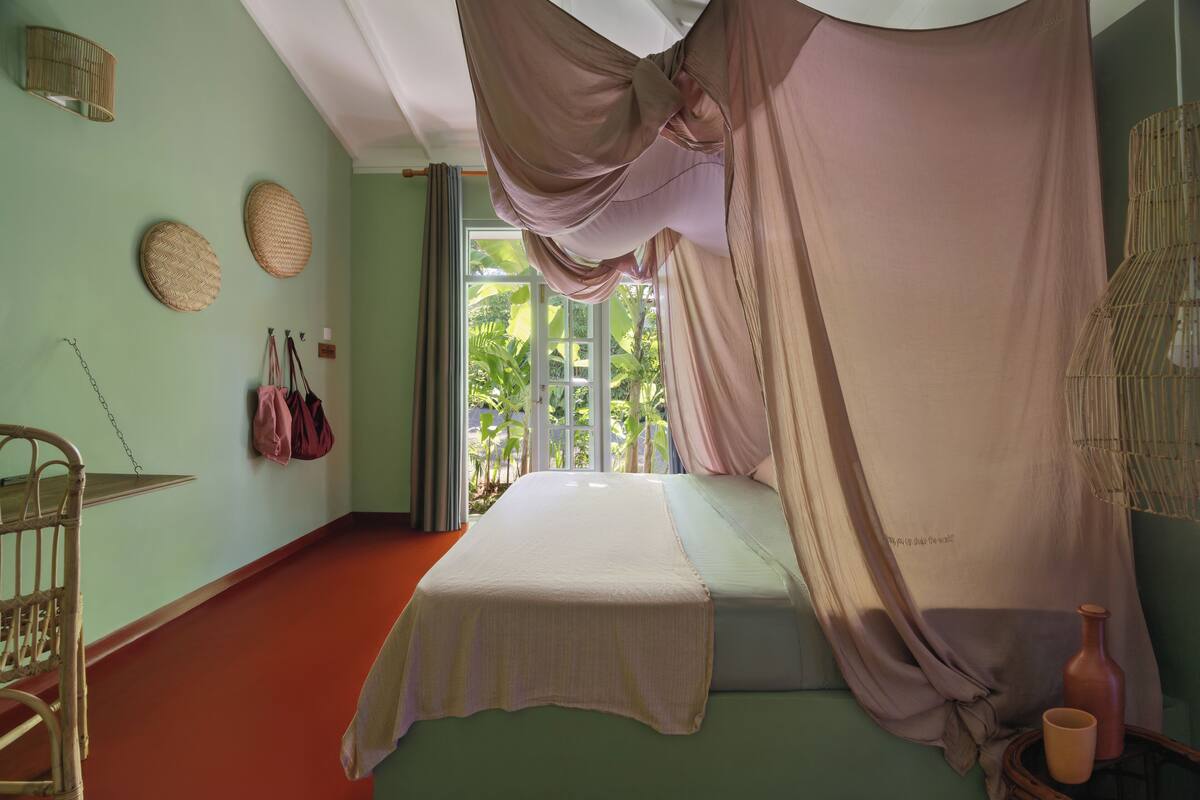 Una habitación con una cama, una silla, un ventanal con cortinas y una pared decorada con cestas tejidas.