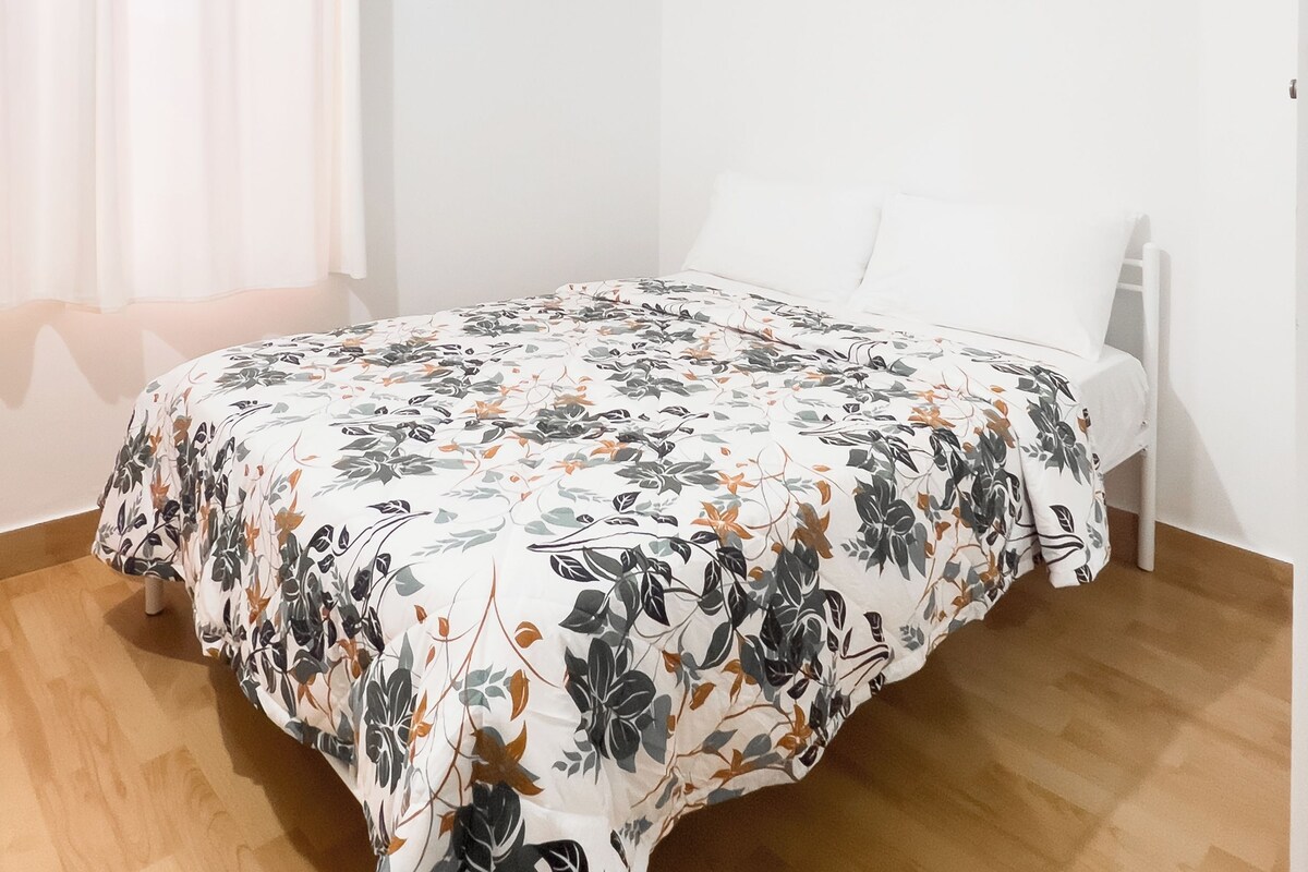 A bedroom with a bed, white walls, a ceiling fan, and an air conditioning unit.