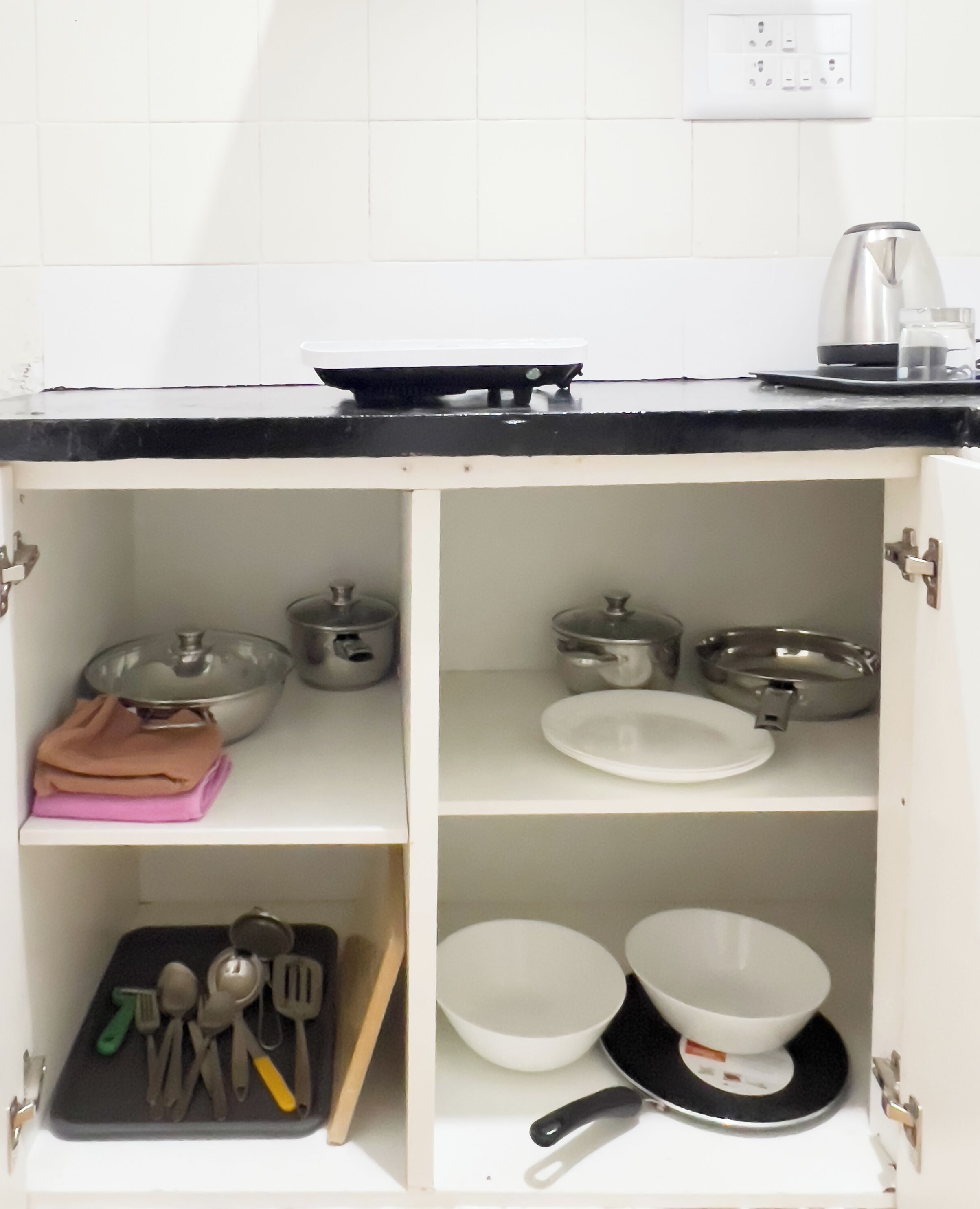 A kitchen with white cabinets, a black countertop, and various kitchen utensils and cookware.