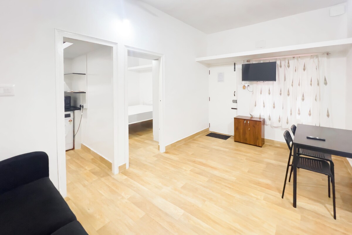 A modern, open-plan living space with a kitchen area, a dining table with chairs, and a black sofa.