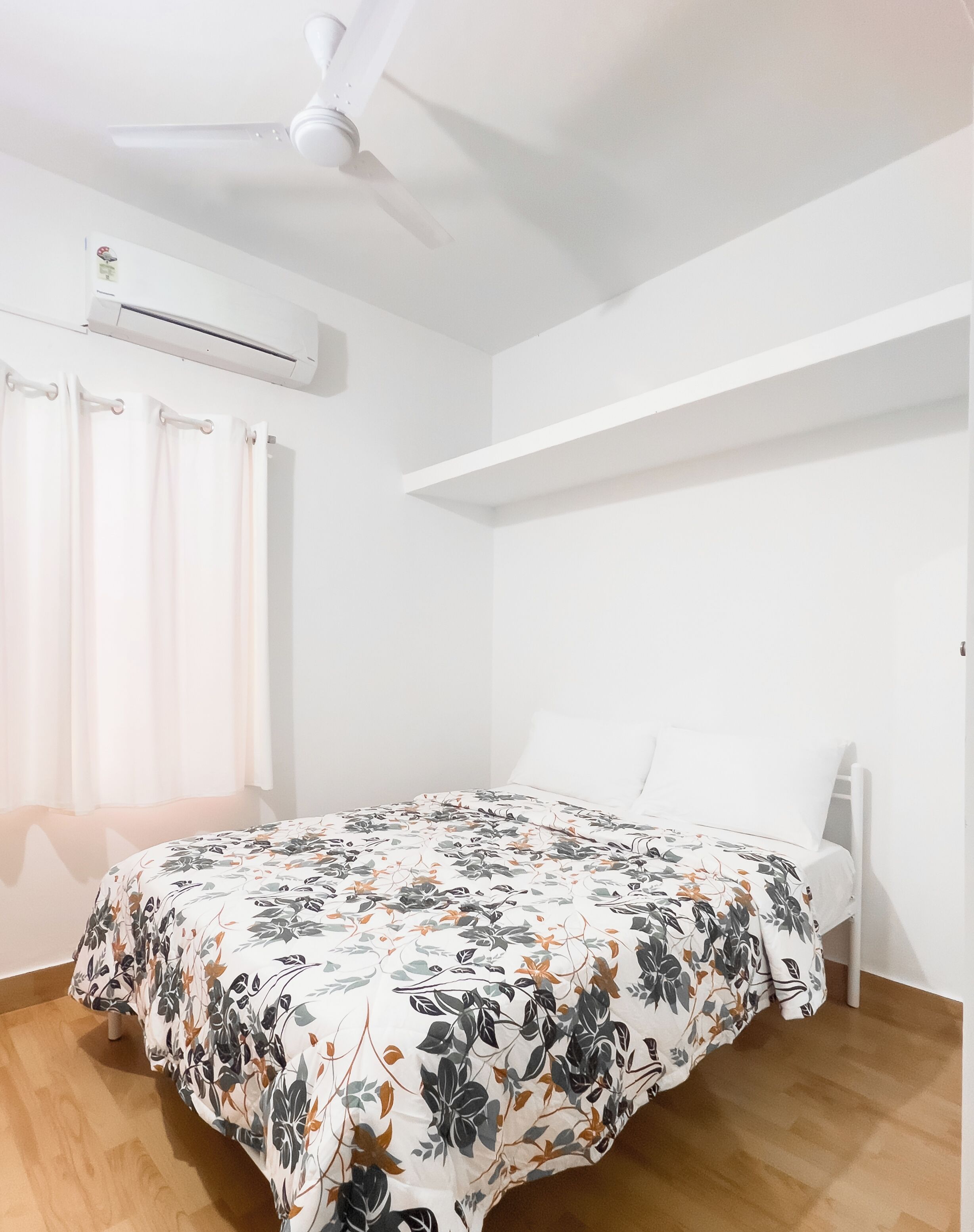 A bedroom with a bed, an air conditioning unit, a ceiling fan, and a window with curtains.