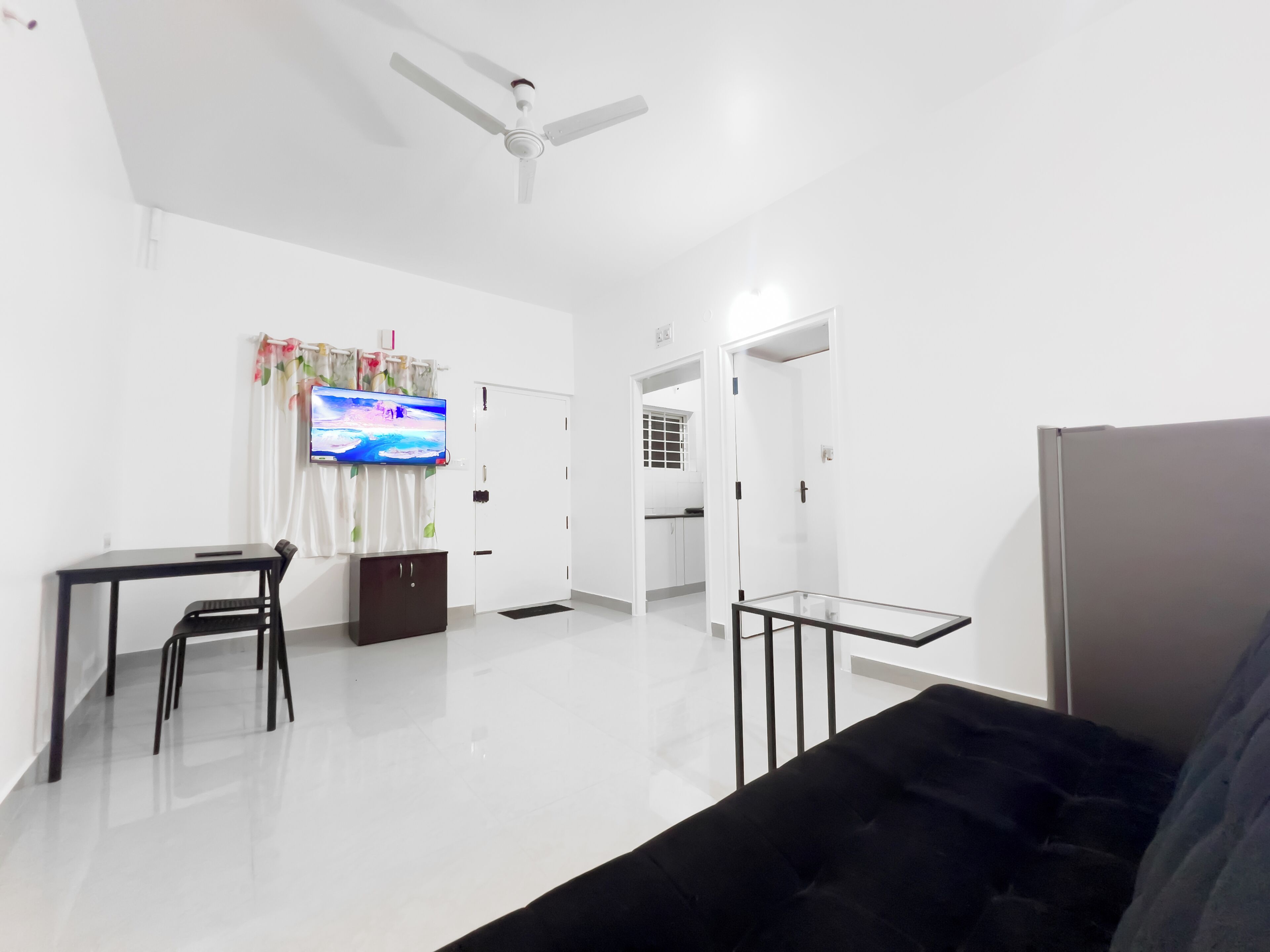 A modern living room with a flat-screen TV, a ceiling fan, a sofa, and a dining area with chairs and a table.