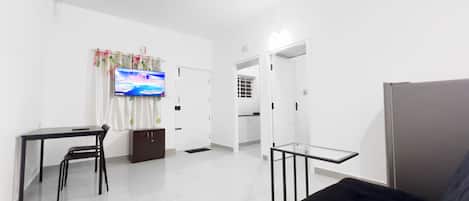 A modern living room with a flat-screen TV, a ceiling fan, a sofa, and a dining area with chairs and a table.