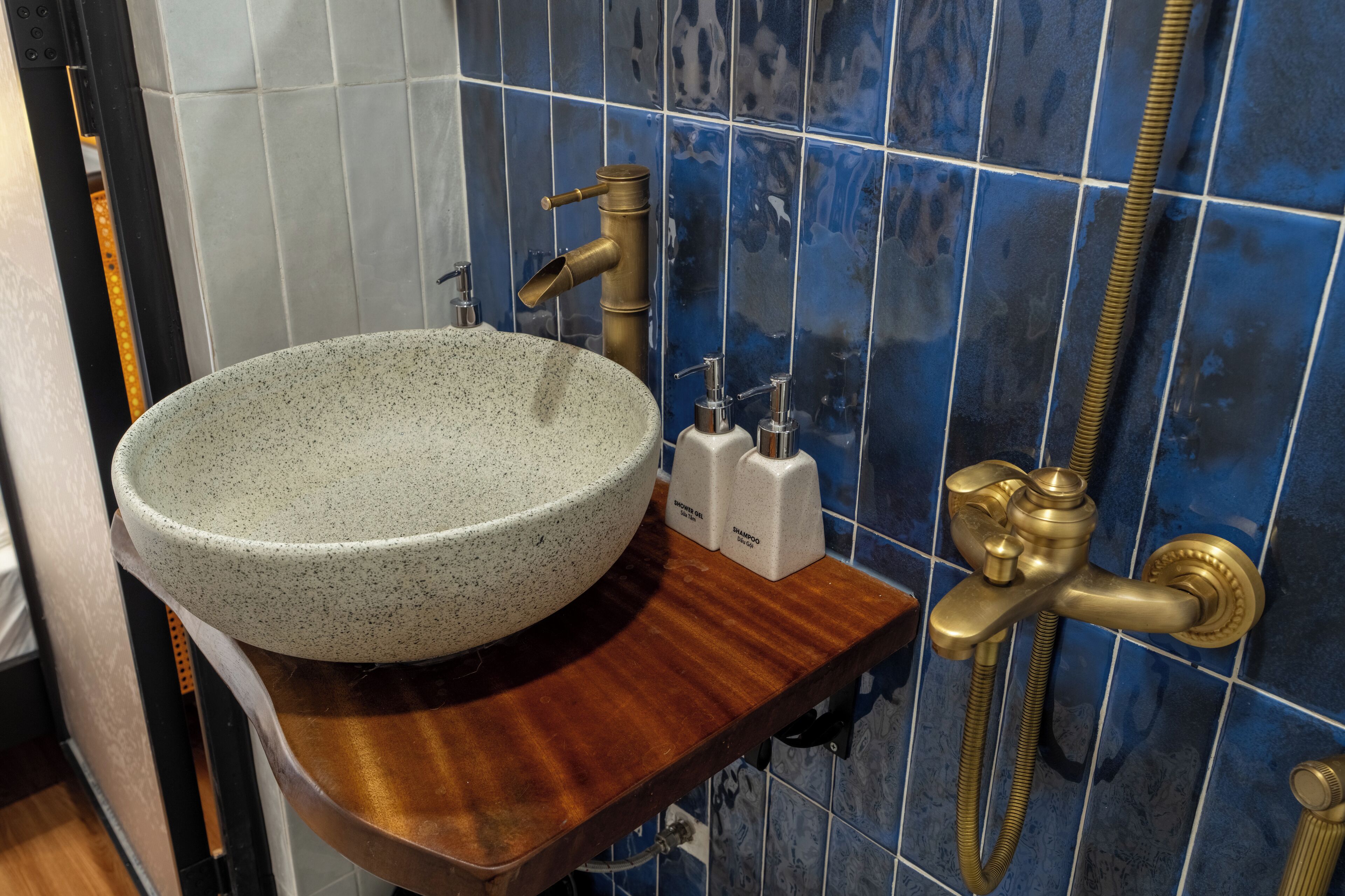 A bathroom with a large speckled sink, a wooden countertop, a gold showerhead, and blue-tiled walls.