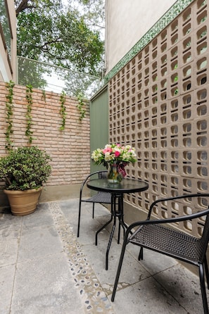 Un pequeño espacio al aire libre con mesa y sillas, una planta en maceta y un muro decorativo.