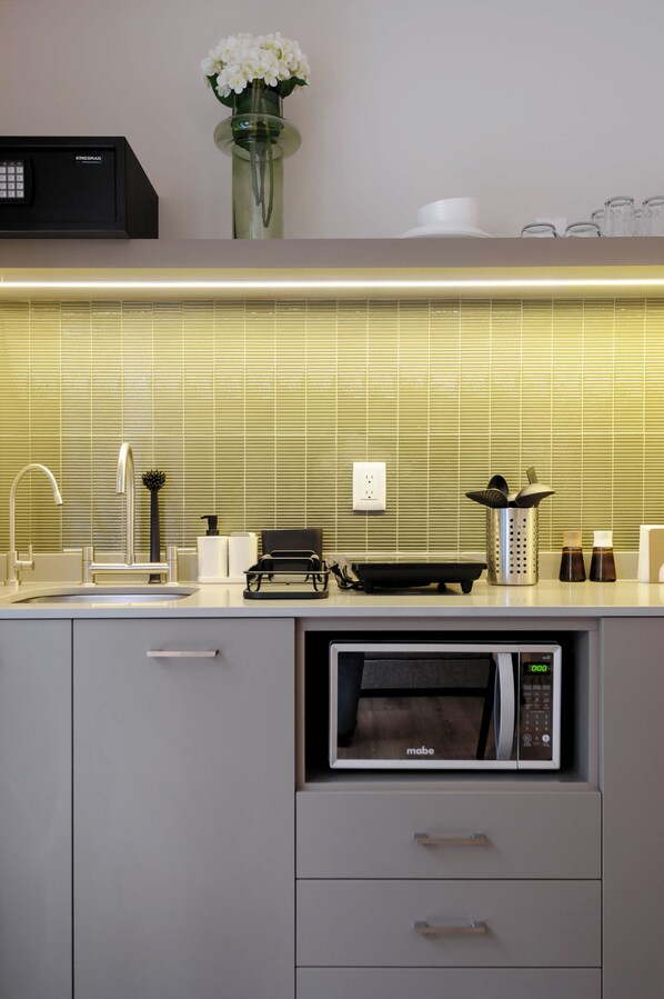 Una cocina compacta con microondas integrado, un lavamanos pequeño y una estufa compacta.