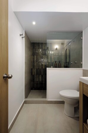 Un baño moderno con cabina de ducha de vidrio, inodoro y tocador con espejo.